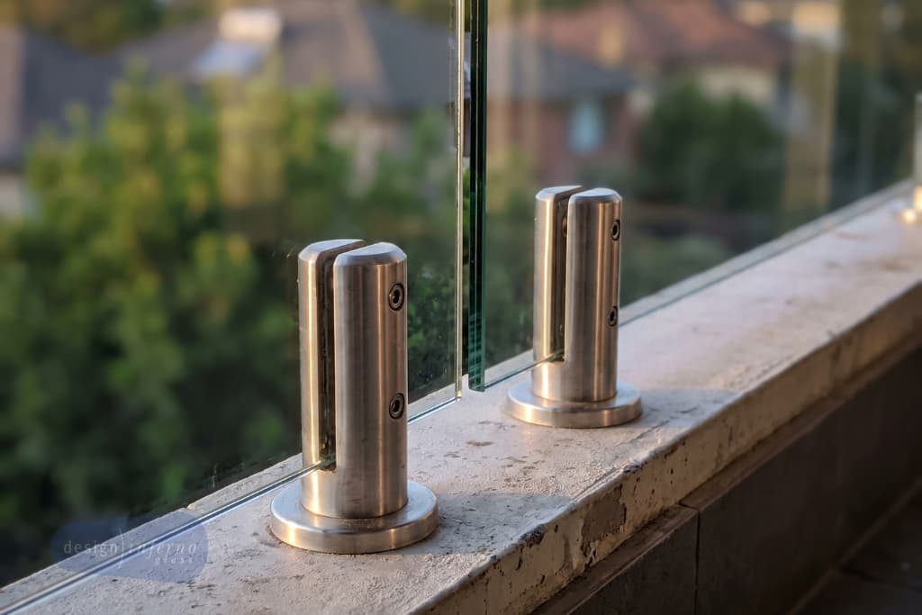 Close up of polished stainless steel spigots holding a frameless glass balustrade panel on a balcony